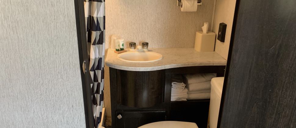 Bathroom in camper with dark wooden cabinets, cream sink and toilet, and black, white, and tan shower curtain